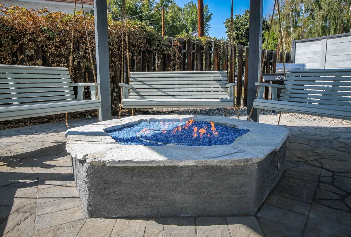 A welcoming backyard gathering area with a central fire pit surrounded by swing benches, set against the backdrop of a sunset. The scene hints at evenings spent socializing, sharing stories, and winding down after a day of exploration.