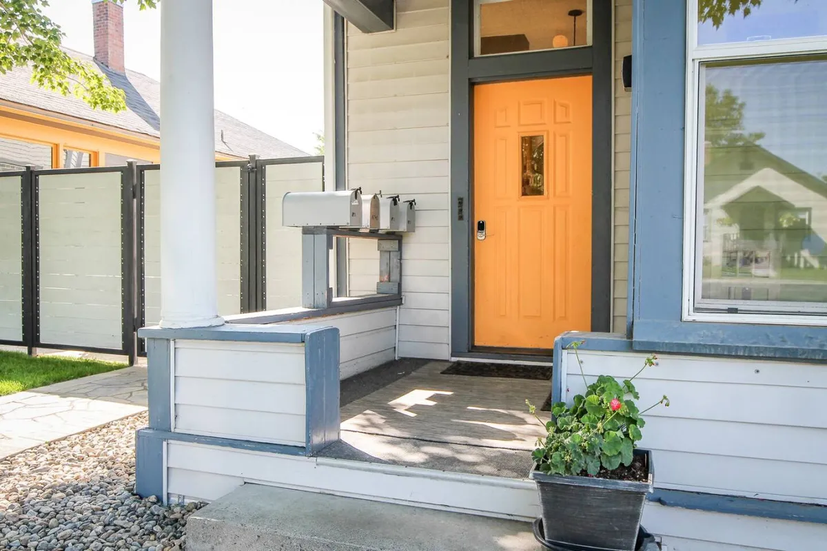 The exterior of Palmer House is showcased with a bright orange front door, a welcoming mailbox, and colorful planters full of flowers. The scene feels inviting and hints at a vibrant, community-oriented atmosphere, perfect for accessing nearby culinary experiences.