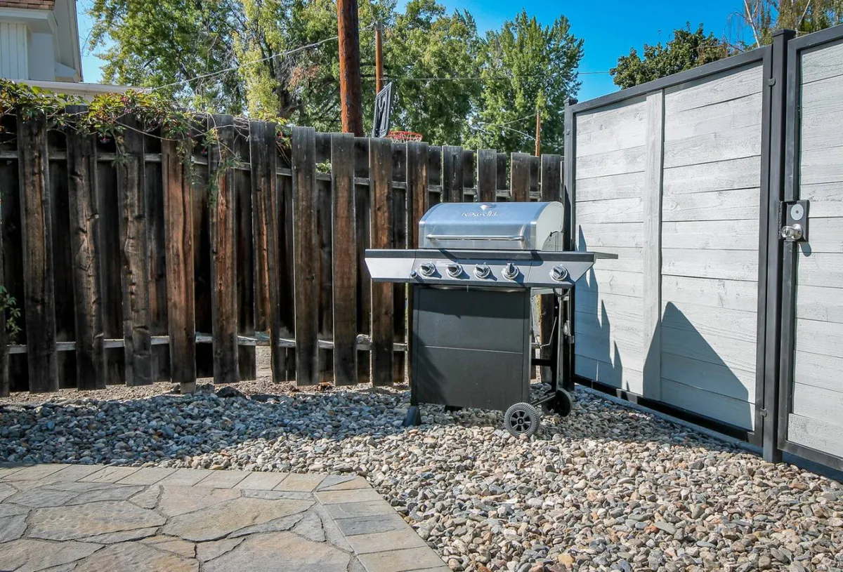 A welcoming exterior patio with a grill, stone patio area, and a wooden fence, designed for outdoor dining and group gatherings. The setting evokes a relaxed mood, ideal for evening barbecues or social occasions.
