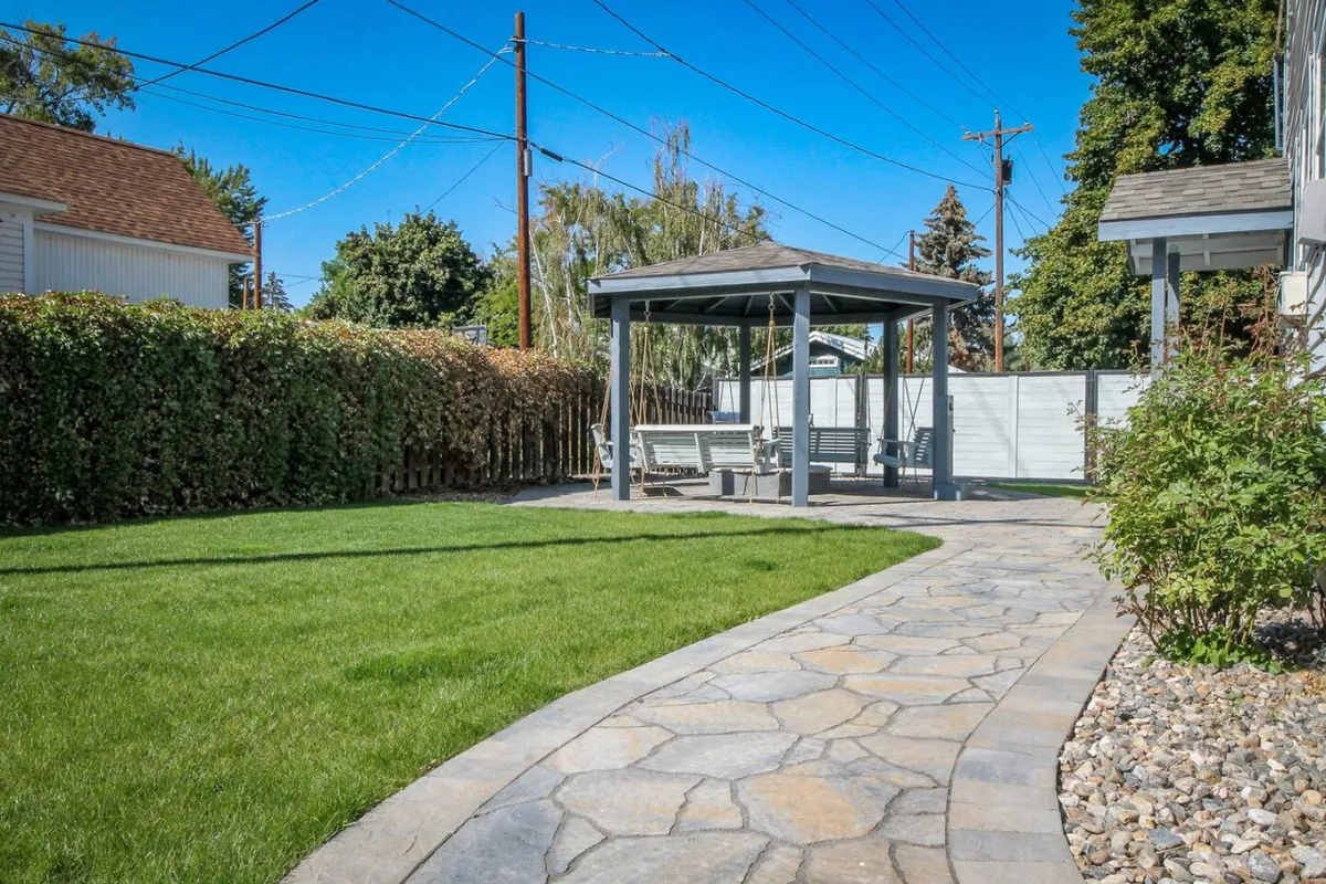 A lush green lawn is bordered by a hedge and anchored by a pergola, with a stone pathway leading into the space. The scene is tranquil and natural, providing a more secluded nook perfect for quiet contemplation or enjoying morning coffee surrounded by greenery.