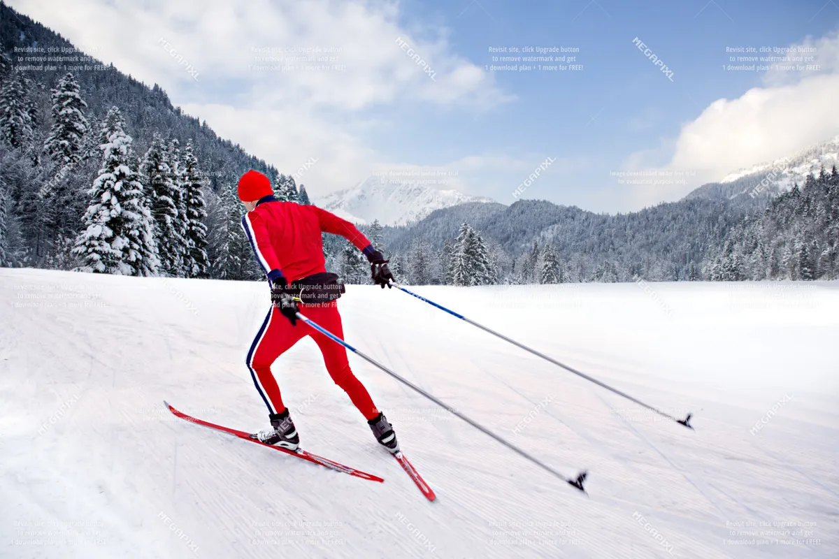 A skier in vivid red attire carves a path across a snow-blanketed landscape, framed by distant mountains and clusters of pine trees. The scene is energetic, capturing both the thrill of winter sports and the natural beauty of the mountains surrounding Anthony Lakes.