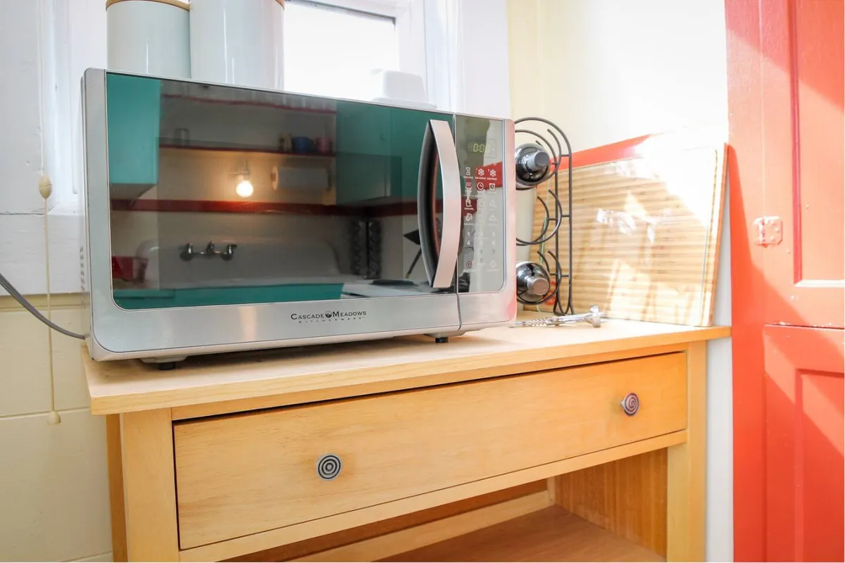 A thoughtfully arranged kitchen corner with a microwave, wooden drawer, and striking red door. Modern appliances blend with warm accents, creating an inviting atmosphere for preparing quick snacks or morning coffee.