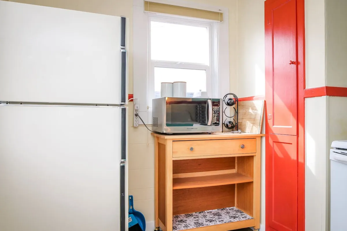 This image captures a compact kitchen scene featuring a white refrigerator, microwave, wooden cart, and red cabinet. The layout demonstrates efficient use of space and hints at the kitchen’s role as a center for shared meals and intimate gatherings.