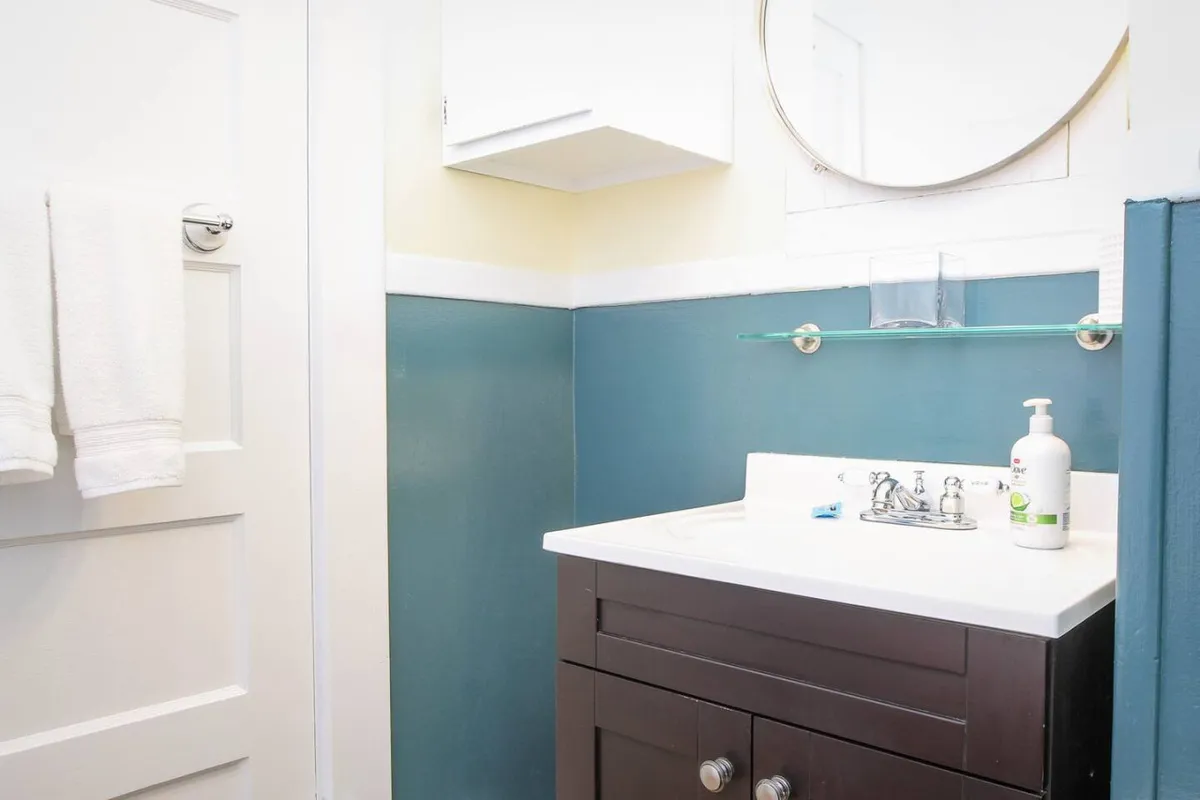 A charming bathroom vanity area is showcased, with a pedestal sink, elegant mirror, and towel rack illuminated by natural light. The tidy arrangement and soothing color palette lend an air of vintage luxury and comfort. The scene highlights the space's potential for morning routines and self-care.