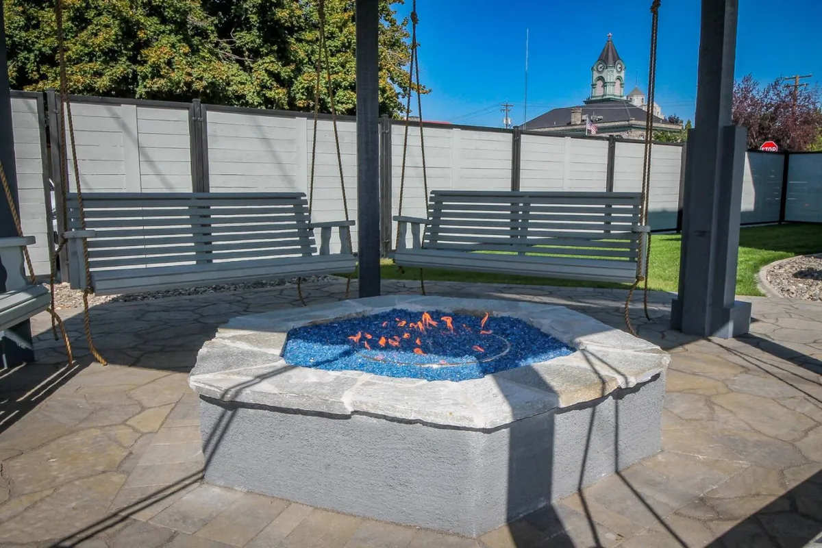 A cozy outdoor fire pit area with hanging swings surrounded by lush greenery, creating a comfortable social space ideal for relaxing after a day of exploring local food and drink spots.